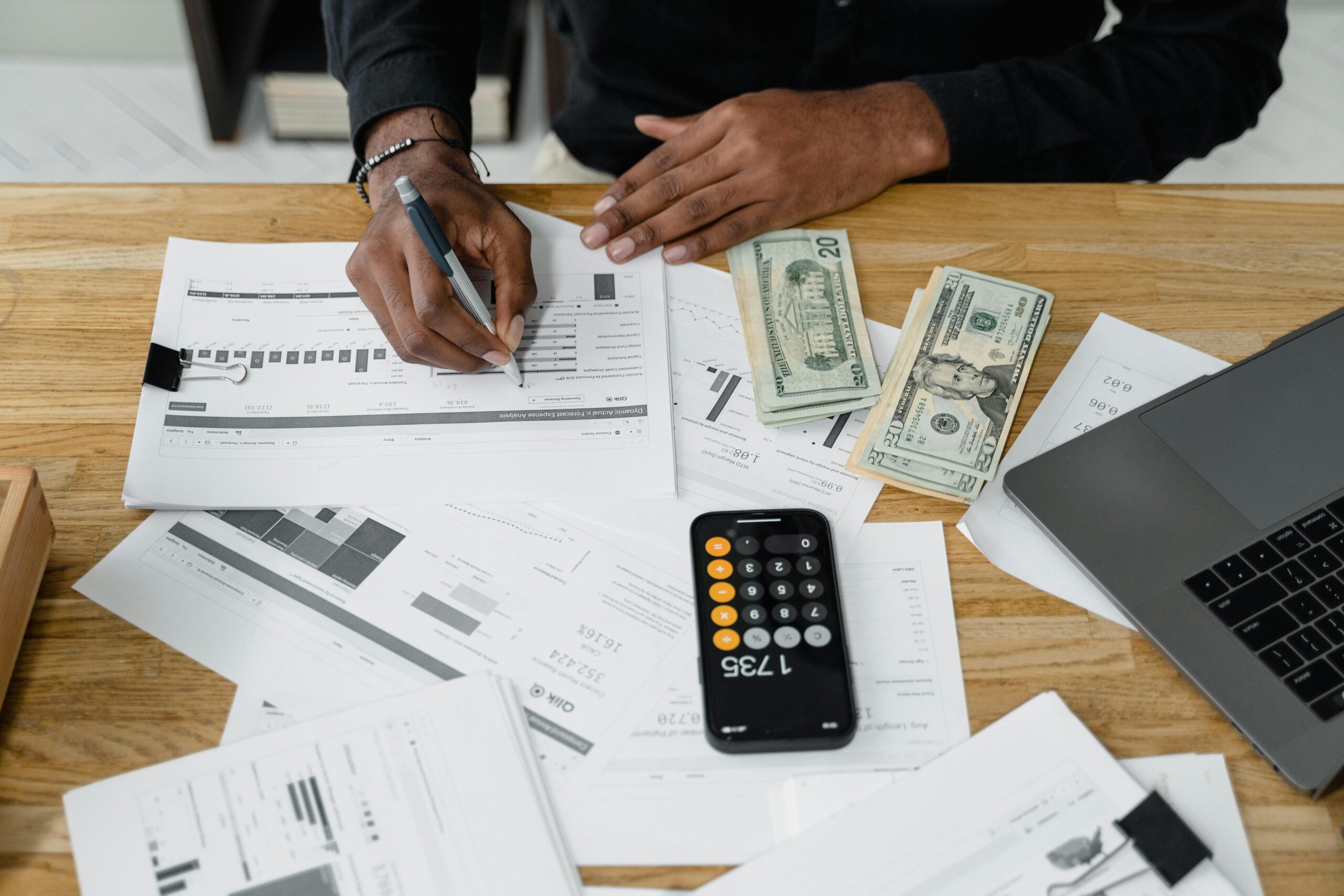 pexels photo 6694492 6694492 Man working on financial reports with calculator, money, and laptop on a desk.